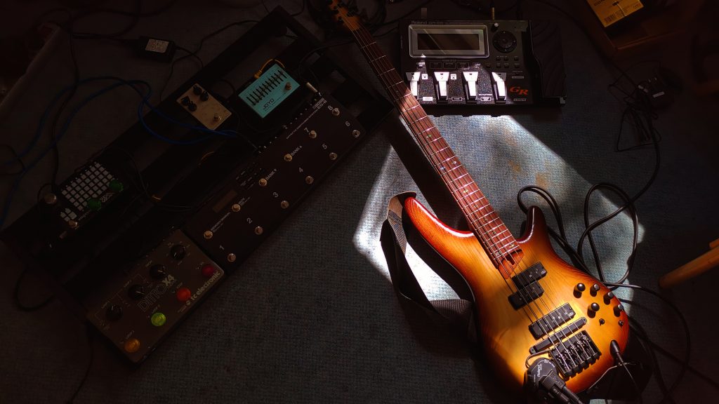 banez Bass lying on a floor next to pedalboard and loopstation with light shining through a window